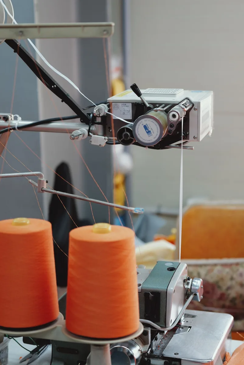 Close-up of an industrial sewing machine with orange thread spools.
